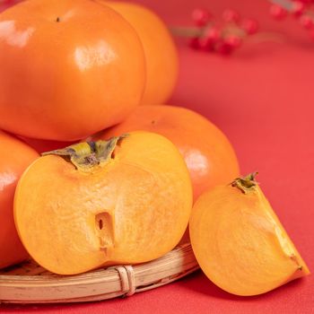 Fresh beautiful sliced sweet persimmon kaki isolated on red table background and bamboo sieve, Chinese lunar new year design concept, close up.