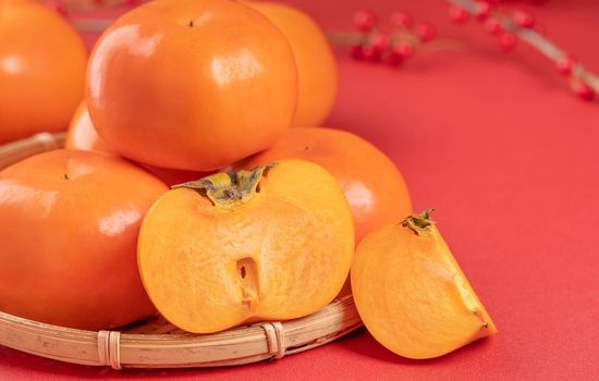 Fresh beautiful sliced sweet persimmon kaki isolated on red table background and bamboo sieve, Chinese lunar new year design concept, close up.