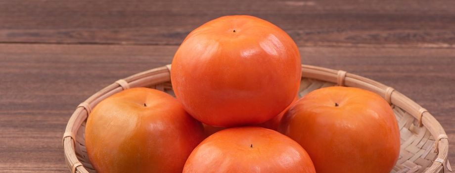 Fresh, beautiful orange color persimmon kaki on bamboo sieve over dark wooden table. Seasonal, traditional fruit of Chinese lunar new year, close up.