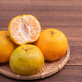 Fresh, beautiful orange color tangerine on bamboo sieve over dark wooden table. Seasonal, traditional fruit of Chinese lunar new year, close up.