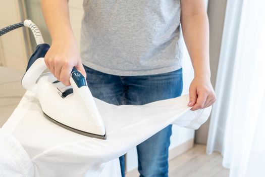Woman ironing sleeve of white shirt with much steam on ironing board