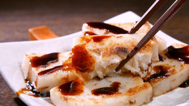 Pouring black soy sauce on ready-to-eat delicious turnip cake, Chinese traditional local dish radish cake in restaurant, close up, copy space.