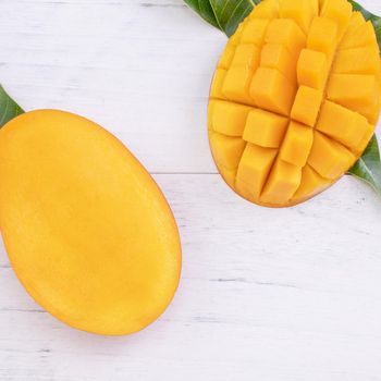 Beautiful chopped ripe mango with green leaves on bright white color wooden background, top view, flat lay, copy space. Tropical fruit design concept.