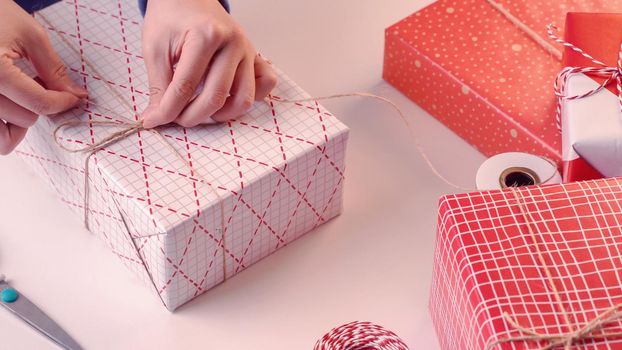 A young woman in blue is wrapping, packaging Christmas gift for kids children by beautiful, red, white wrapper with glittering light, lifestyle.