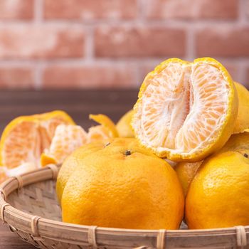 Peeled tangerines in a bamboo sieve basket on dark wooden table with red brick wall background, Chinese lunar new year fruit design concept, close up.