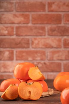 Sliced sweet persimmon kaki in a bamboo sieve basket on dark wooden table with red brick wall background, Chinese lunar new year fruit design concept, close up.