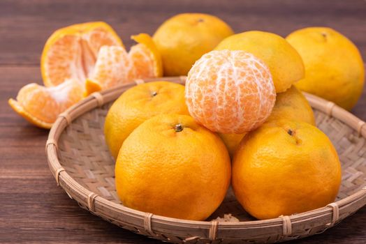 Fresh, beautiful orange color tangerine on bamboo sieve over dark wooden table. Seasonal, traditional fruit of Chinese lunar new year, close up.