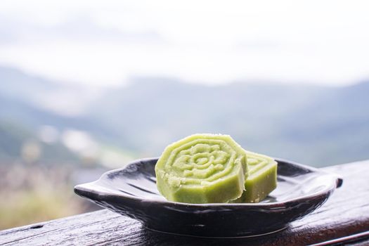 Delicious green mung bean cake with black tea plate on wooden railing of a teahouse in Taiwan with beautiful landscape in background, close up.