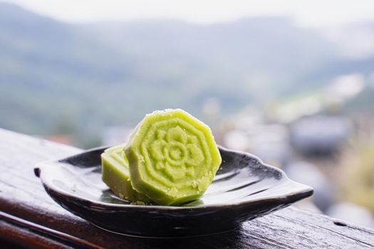 Delicious green mung bean cake with black tea plate on wooden railing of a teahouse in Taiwan with beautiful landscape in background, close up.