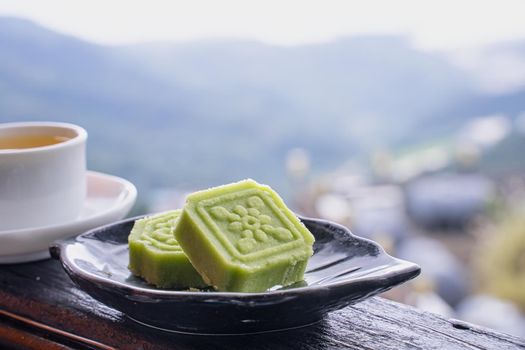 Delicious green mung bean cake with black tea plate on wooden railing of a teahouse in Taiwan with beautiful landscape in background, close up.