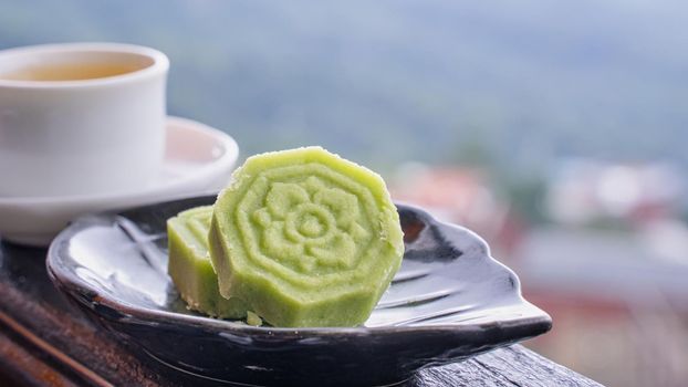 Delicious green mung bean cake with black tea plate on wooden railing of a teahouse in Taiwan with beautiful landscape in background, close up.