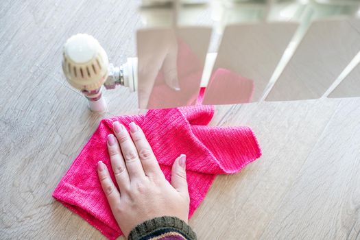 Female hand with rag cleaning water from heating radiator