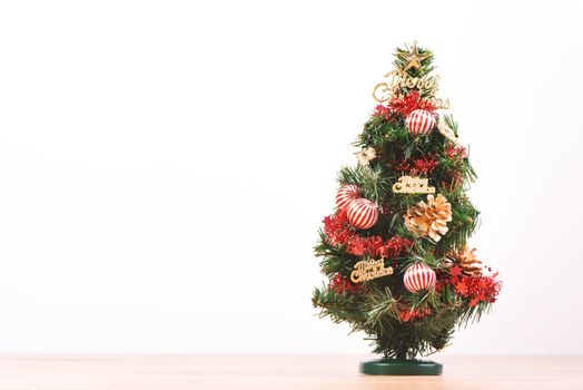 Decorated cute Christmas tree on a wooden floor with white background and toys, blank for festive design concept, close up.