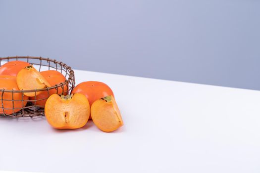 Fresh beautiful sliced sweet persimmon kaki isolated on white kitchen table with gray blue background, Chinese lunar new year design concept, close up.