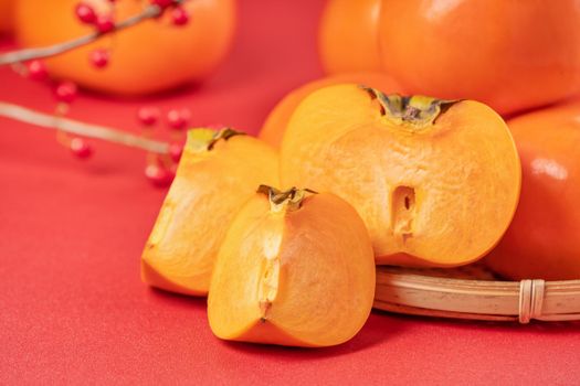 Fresh beautiful sliced sweet persimmon kaki isolated on red table background and bamboo sieve, Chinese lunar new year design concept, close up.