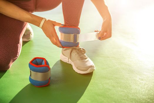 Woman putting on ankle wights before she starts a workout in a gym, health and fitness