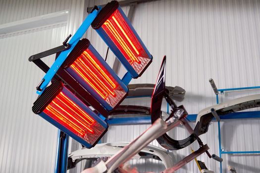 Painting and drying under lamps in professional box of car body parts after applying paint on bumper