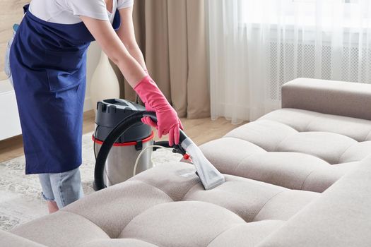 Woman Cleaning Sofa With Vacuum Cleaner At Home