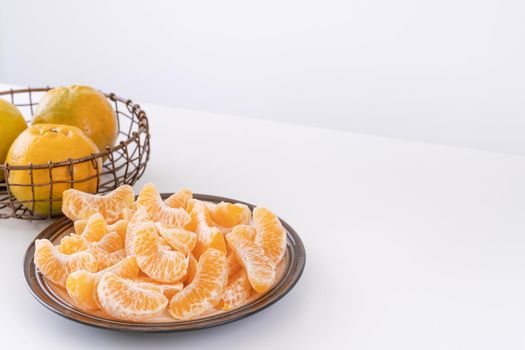 Beautiful peeled tangerines in a plate and metal basket isolated on bright white clean table in a modern contemporary kitchen island, close up.