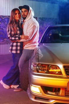 Smiling loving couple standing near sport car over night city background