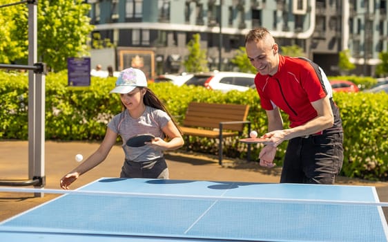 Family playing table tennis outside house.