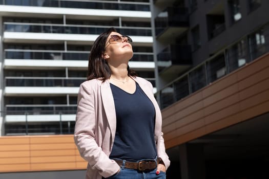 Happy Mature 40 yo Woman Enjoys View Of New Apartment Campus, Complex In Daytime. Female Brunette Wears Casual Cloth, Looks At Construction, Modern Residential Building, Horizontal Plane.