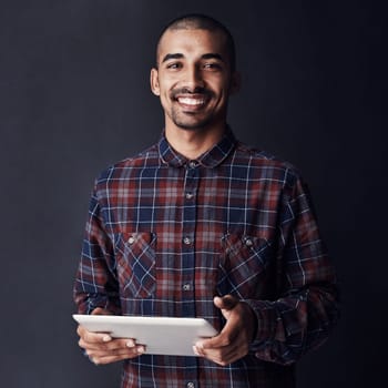 Cool, calm and connected. Studio portrait of a young man using a digital tablet against a dark background