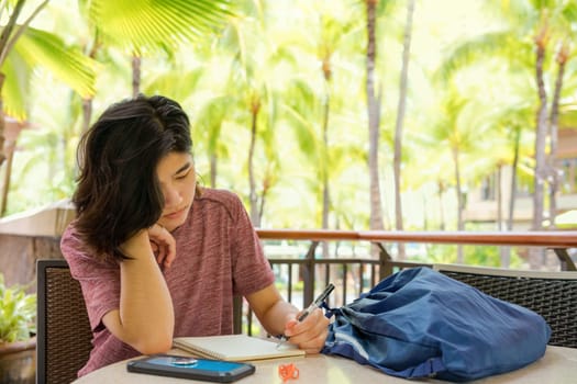 Young woman writing in notebook outdoors in tropical location with palm trees in sunny background