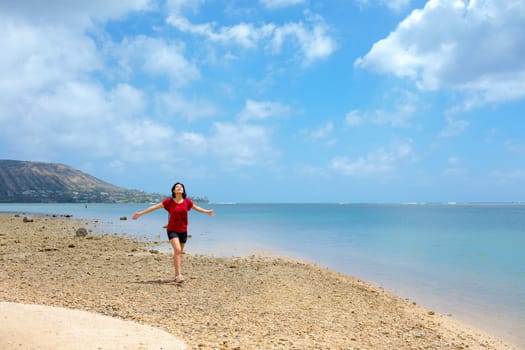 Young woman enjoying walk on empty beach by quiet bay on Oahu, Hawaii with Kokohead Crater in background