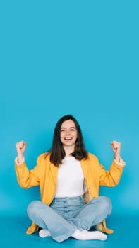 Vibrant Portrait of a Joyful Girl Celebrating Success with Raised Fists and a Victorious 'Yes ' - Isolated on Blue Background - Positive, Optimistic Emotions.