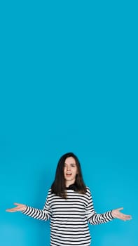 Captivating Portrait of Astonished Woman in Striped Pullover - Surprised and Amazed Female Model with Arms Extended - Isolated on Blue Background - Perfect for Expressing Shock, Surprise, and Emotion.