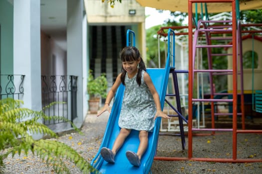 Happy girl playing on the slide. Happy little asian girl sliding and playing at outdoor playground in park on summer vacation. Healthy activity.