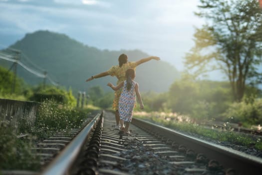 Mother and cute daughter walking on the railroad in the daytime. Happy family walking on the railway against the background of mountains and greenery.