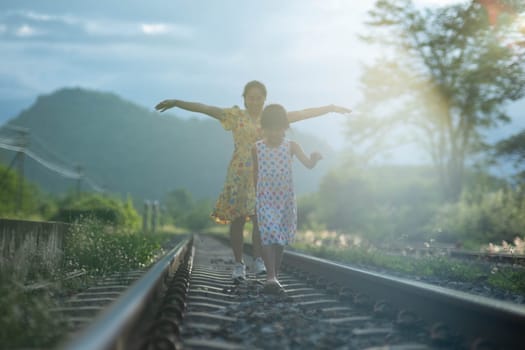Mother and cute daughter walking on the railroad in the daytime. Happy family walking on the railway against the background of mountains and greenery.