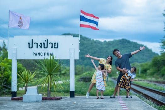 8 June 2023: Lampang, Thailand - Happy family taking pictures together at Pang Puai Railway Station against a background of green mountains and trees.