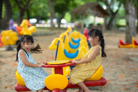 Children sit on a carousel in the playground together. Children playing at outdoor playground in the park on summer vacation. Healthy activity.