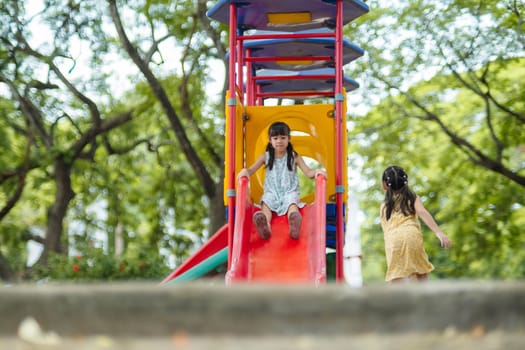 Happy girl having fun on colorful slides. Children playing slides at outdoor playground in park during summer vacation. Healthy activity.