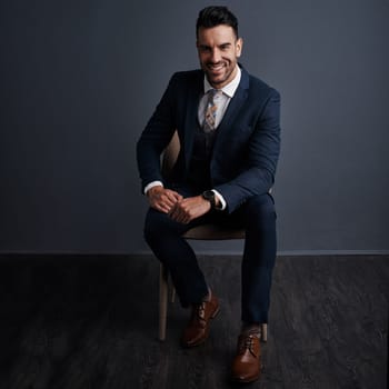 Stay motivated and make things happen. Studio shot of a stylish young businessman sitting on a chair against a gray background