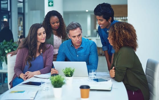 Using online tools for a better outcome. a group of designers gathering around a man using a laptop in a meeting