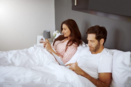 This relationship is getting old. a couple using their wireless devices while lying in bed