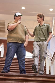 Student, teenager friends and boys walking down university and school steps with a smile. Conversation, talking and discussion of guy group feeing happy on education building stairs with a talk.