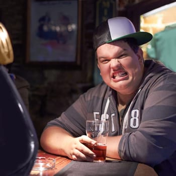 Plus size, man and silly face at a pub with a beer drink feeling funny with comedy. Male person, crazy portrait and alcoholic at a restaurant and club by counter with alcohol and cool style alone.