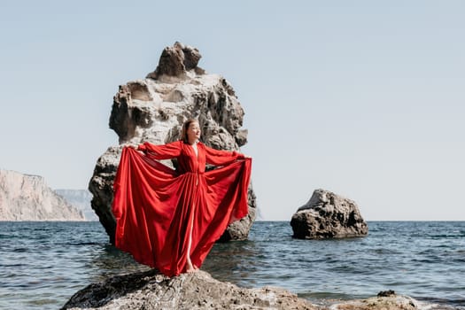 Woman travel sea. Young Happy woman in a long red dress posing on a beach near the sea on background of volcanic rocks, like in Iceland, sharing travel adventure journey