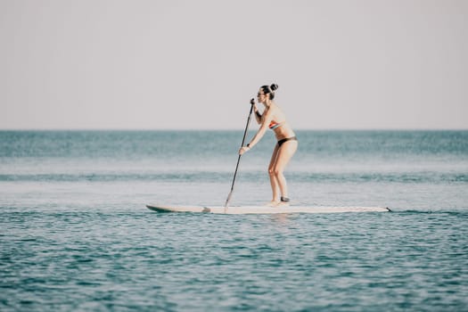 Sea woman sup. Silhouette of happy middle aged woman in rainbow bikini, surfing on SUP board, confident paddling through water surface. Idyllic sunset. Active lifestyle at sea or river