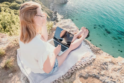 Woman sea laptop. Business woman in yellow hat working on laptop by sea. Close up on hands of pretty lady typing on computer outdoors summer day. Freelance, digital nomad, travel and holidays concept.