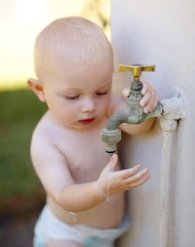 Outdoor, water and a baby playing at a tap in a summer garden at home. Little kid, childhood growth and adorable infant boy curious about faucet, washing hands and getting wet in backyard of a house.