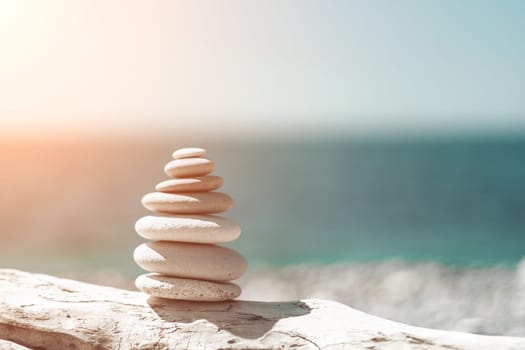 Balanced Pebbles Pyramid on the Beach on Sunny Day and Clear Sky at Sunset. Blue Sea on Background Selective focus, zen stones on sea beach, meditation, spa, harmony, calm, balance concept.