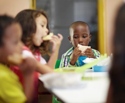 Eating, boy and children class for lunch at school or creche for an education or to learn. Break, kid and sandwich in a classroom to eat or learning or hungry at desk for nutrition with friends