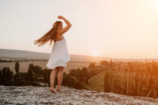 Romantic beautiful bride in white dress posing with sea and mountains in background. Stylish bride standing back on beautiful landscape of sea and mountains on sunset