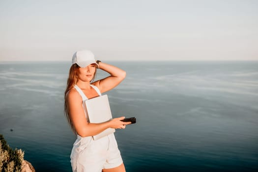 Digital nomad, Business woman working on laptop by the sea. Pretty lady typing on computer by the sea at sunset, makes a business transaction online from a distance. Freelance, remote work on vacation